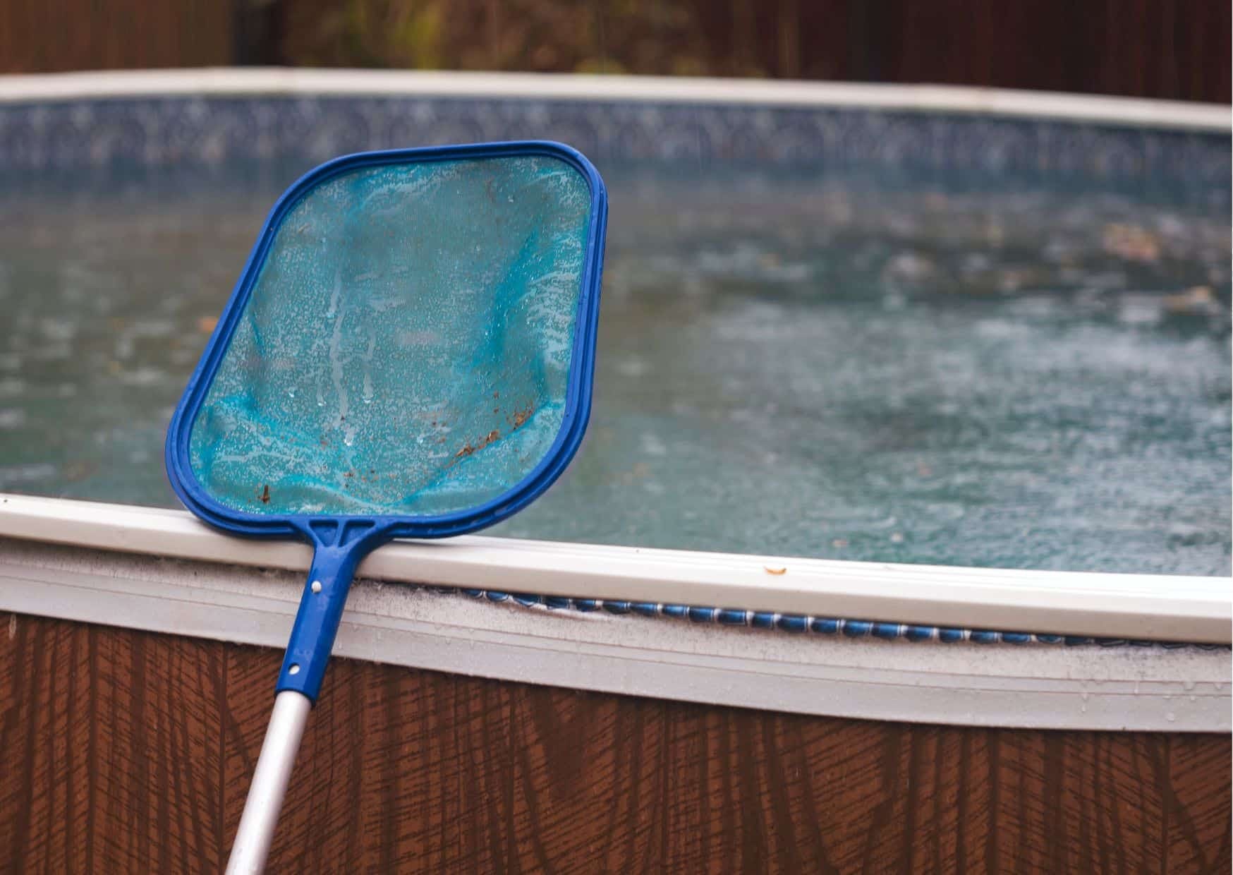 Retino blu appoggiato al bordo di una piscina fuori terra con acqua sporca e detriti in superficie, utilizzato per la corretta pulizia della piscina